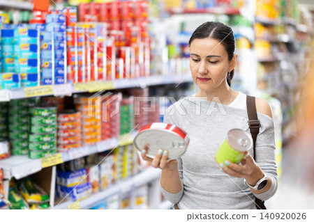 Woman customer in supermarket choose canned food, buy food stuff in grocery store Woman customer in supermarket choose canned food, buy food stuff in grocery store 140920026
