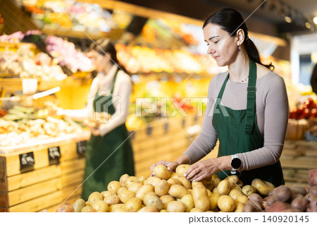 Female seller laying out potatoes on the counter Female seller laying out potatoes on the counter 140920145