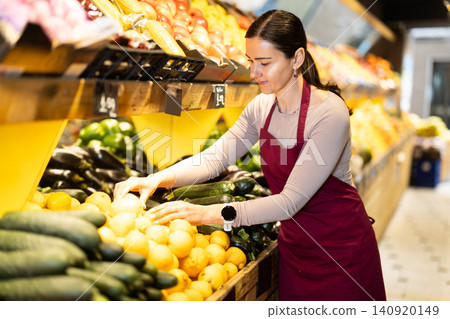 Female salesperson carefully places ripe lemons on the counter of grocery supermarket Female salesperson carefully places ripe lemons on the counter of grocery supermarket 140920149