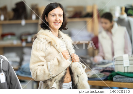 Woman try on fur jacket in front of mirror in clothes store Woman try on fur jacket in front of mirror in clothes store 140920150
