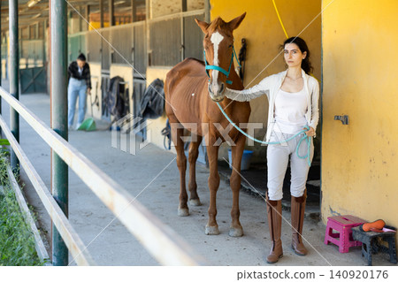 Armenian female worker takes horse out of stall, holds animal by bridle and leads pet for walk Armenian female worker takes horse out of stall, holds animal by bridle and leads pet for walk 140920176