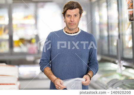 Adult man with plastic bag choosing groceries in store Adult man with plastic bag choosing groceries in store 140920200
