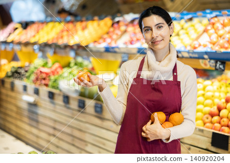 Young woman seller offers tangerines in vegetable shop Young woman seller offers tangerines in vegetable shop 140920204