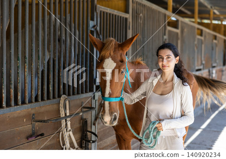 Armenian female worker takes horse out of stall, holds animal by bridle and leads pet for walk 140920234