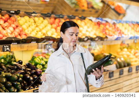 Female shopper carefully selecting ripe zucchini in supermarket Female shopper carefully selecting ripe zucchini in supermarket 140920341