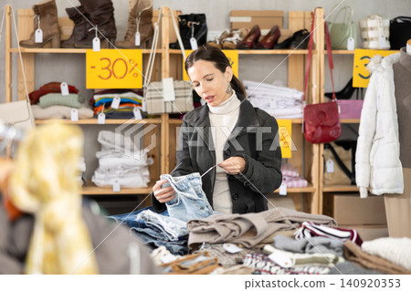 Attentive middle-aged woman choosing jean pantaloons in clothing store Attentive middle-aged woman choosing jean pantaloons in clothing store 140920353