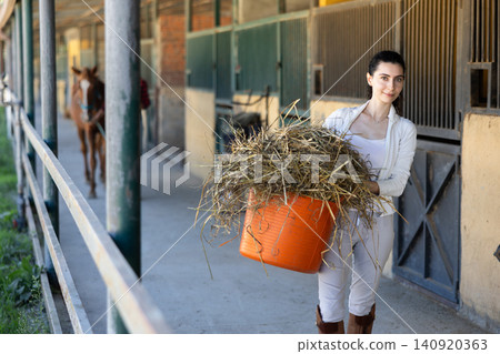 Young woman with bucket of hay in stable 140920363