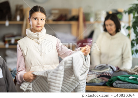 Teen girl looks at products in store and selects coat or jacket. Family shopping Teen girl looks at products in store and selects coat or jacket. Family shopping 140920364