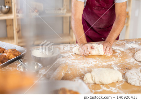 Unrecognizable senior man works in bakery as baker, kneads dough, works with flour. Unrecognizable senior man works in bakery as baker, kneads dough, works with flour. 140920415