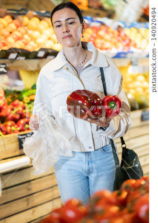 Focused positive middle aged woman shopping in organic food store, choosing bell peppers Focused positive middle aged woman shopping in organic food store, choosing bell peppers 140920494