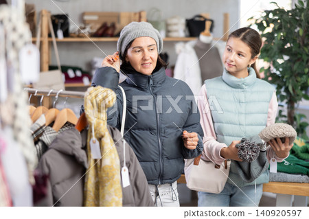 Woman with girl trying on winter hat in store, family shopping with daughter. Woman with girl trying on winter hat in store, family shopping with daughter. 140920597