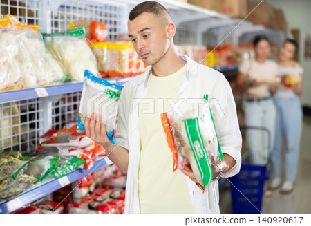 Man comparing different noodle packages in Asian grocery store Man comparing different noodle packages in Asian grocery store 140920617