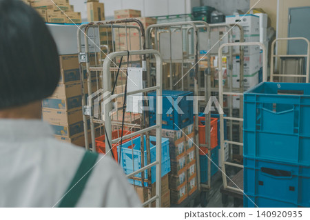 A staff member's back is seen inspecting a warehouse in the back room of a supermarket, where rolling carts are lined up. A staff member's back is seen inspecting a warehouse in the back room of a supermarket, where rolling carts are lined up. 140920935