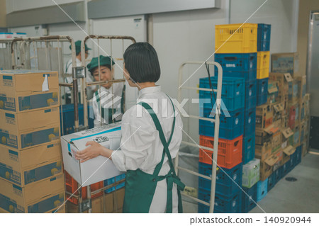 The back view of a female staff member carrying goods in the back room of a supermarket. The back view of a female staff member carrying goods in the back room of a supermarket. 140920944
