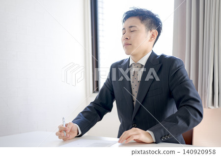 一位年輕的商人工作時深深吸了一口氣。 一位年輕的商人工作時深深吸了一口氣。 140920958