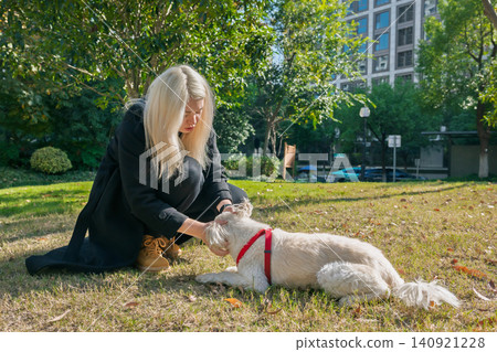 Young woman in black outfit gently offers a treat to her fluffy white dog lying on the green grass in a bright urban park Young woman in black outfit gently offers a treat to her fluffy white dog lying on the green grass in a bright urban park 140921228