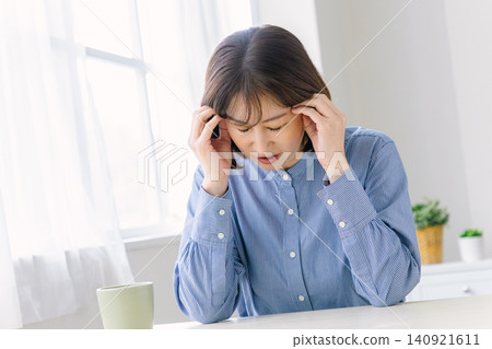 一位中年婦女痛苦地摀著太陽穴。 一位中年婦女痛苦地摀著太陽穴。 140921611