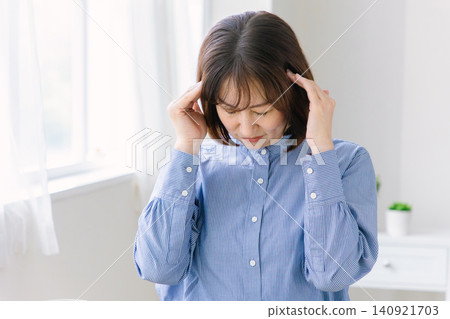 A middle-aged woman clutches her temples with a pained expression. A middle-aged woman clutches her temples with a pained expression. 140921703