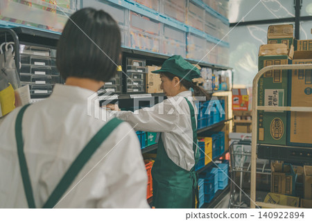 Two female staff members are organizing order slips on shelves in the back room. Two female staff members are organizing order slips on shelves in the back room. 140922894