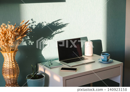 Laptop on desk with notebook and smartphone in home office. Freelancer workspace with plant and cup. Laptop on desk with notebook and smartphone in home office. Freelancer workspace with plant and cup. 140923158