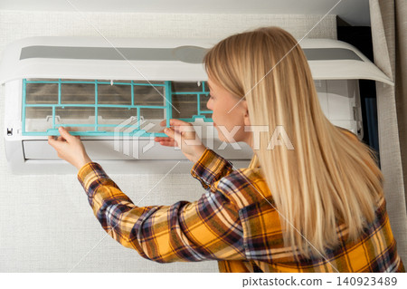Woman replaces air conditioner filter in indoor unit Woman replaces air conditioner filter in indoor unit 140923489
