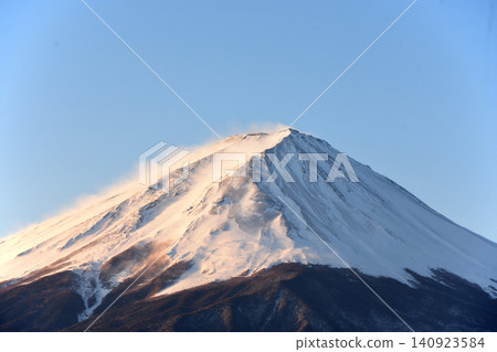 Mount Fuji, completely covered in snow and spewing white plumes of snow, and Mount Komitake, its trees below the treeline covered in snow and appearing grayish in color. Mount Fuji, completely covered in snow and spewing white plumes of snow, and Mount Komitake, its trees below the treeline covered in snow and appearing grayish in color. 140923584
