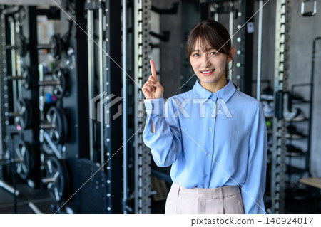 A young woman in office casual attire goes to the gym after work; a woman who works out; goes to the gym; points; guides; trims up 140924017