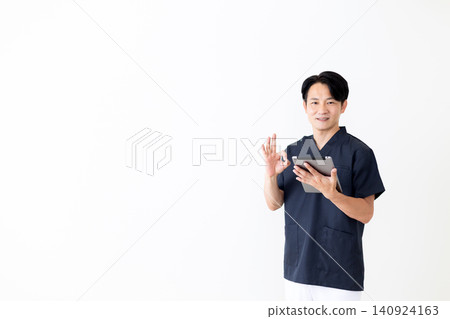 A middle-aged male doctor in navy blue scrubs makes a circular motion while holding a tablet. A middle-aged male doctor in navy blue scrubs makes a circular motion while holding a tablet. 140924163