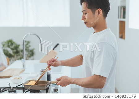 一位年輕男子正在廚房裡煎蛋捲。 一位年輕男子正在廚房裡煎蛋捲。 140925179