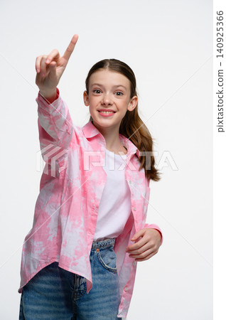 Smiling teenage girl pointing upward while looking at camera. 140925366
