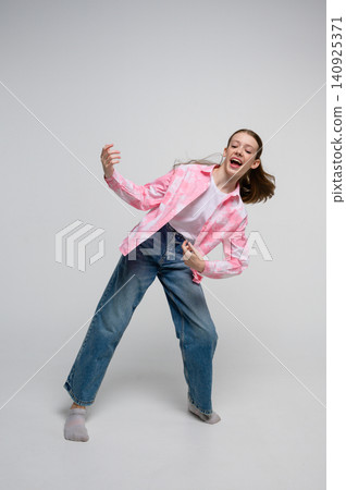 Energetic teenage girl pretending to play air guitar and sing. 140925371