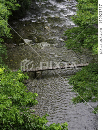 A simple wooden log bridge spanning a clear stream surrounded by lush new greenery. A simple wooden log bridge spanning a clear stream surrounded by lush new greenery. 140925727