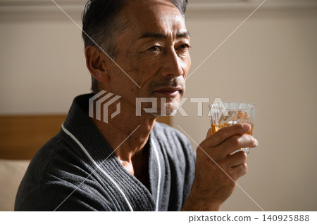 Senior man wearing a gown and holding a rocks glass Lifestyle image 140925888