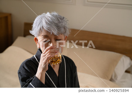 Senior woman wearing a gown and holding a rocks glass Lifestyle image Senior woman wearing a gown and holding a rocks glass Lifestyle image 140925894