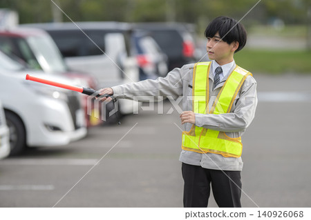 A young security guard directing cars in a parking lot. A young security guard directing cars in a parking lot. 140926068