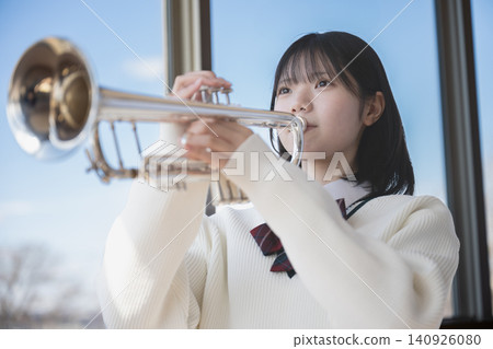 A female student playing the trumpet by the window. A female student playing the trumpet by the window. 140926080