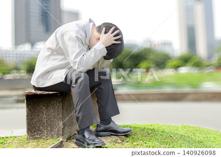 A man in work clothes holding his head in his hands outdoors. A man in work clothes holding his head in his hands outdoors. 140926098