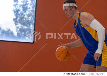 Male basketball player dribbling basketball on gym court, wearing headband, arm sleeve, copy space Male basketball player dribbling basketball on gym court, wearing headband, arm sleeve, copy space 140926493