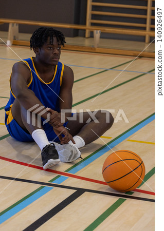 African American adult male sitting in gym wearing blue yellow jersey, orange basketball nearby African American adult male sitting in gym wearing blue yellow jersey, orange basketball nearby 140926497