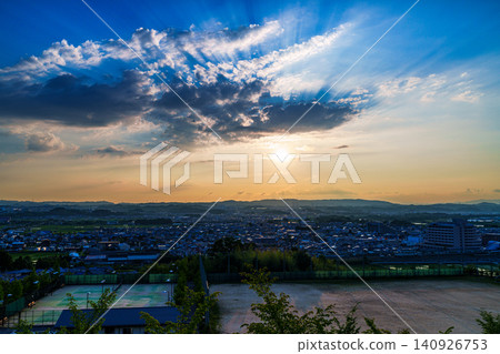 A sunset view from a hill in Minamiyamashiro, southern Kyoto Prefecture: The setting sun casts its light into the sky, painting the mountainside in golden hues. (1) 140926753