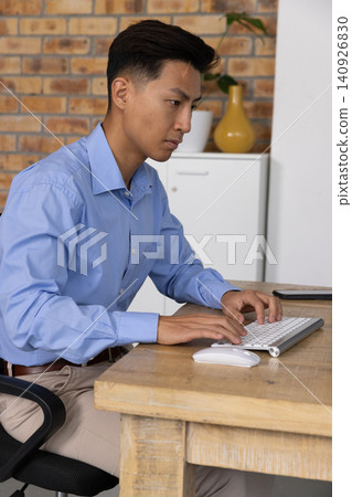 Adult Asian man typing on wireless keyboard at desk in office, wearing light blue shirt Adult Asian man typing on wireless keyboard at desk in office, wearing light blue shirt 140926830