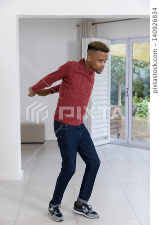 African American man standing in living area near sliding glass door, wearing red sweater and jeans 140926834