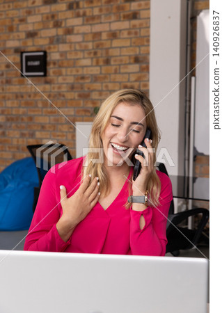 Woman talking on smartphone gesturing at desk with laptop in magenta blouse and wristwatch Woman talking on smartphone gesturing at desk with laptop in magenta blouse and wristwatch 140926837