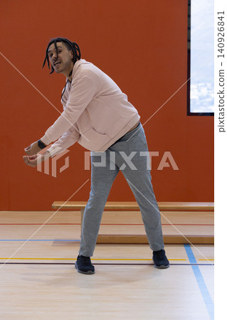 Man wearing light pink zip-up hoodie and grey-sweatpants stretching on gym floor with smartwatch Man wearing light pink zip-up hoodie and grey-sweatpants stretching on gym floor with smartwatch 140926841