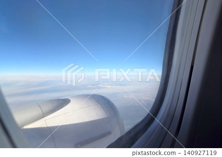 View from an airplane window showing the wing and the sky with clouds during flight over land and mountains in daylight View from an airplane window showing the wing and the sky with clouds during flight over land and mountains in daylight 140927119