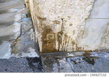 Water flowing from a wall onto the pavement near a corner in an urban area during the day 140927132