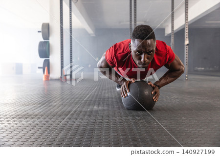 African american man in sportswear doing pushups on medicine ball in gym near cones African american man in sportswear doing pushups on medicine ball in gym near cones 140927199