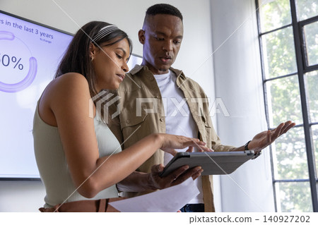 Diverse coworkers reviewing tablet data, pointing at printed paper beside office display screen Diverse coworkers reviewing tablet data, pointing at printed paper beside office display screen 140927202