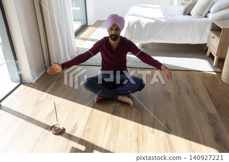 Indian man wearing pink turban and meditating on floor in bedroom, burning incense beside pillows Indian man wearing pink turban and meditating on floor in bedroom, burning incense beside pillows 140927221