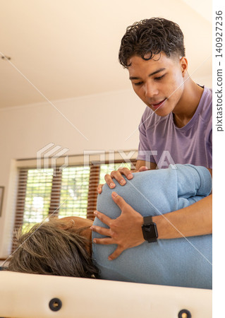 Male therapist performing manual adjustment on Asian senior woman patient on table by window blinds Male therapist performing manual adjustment on Asian senior woman patient on table by window blinds 140927236